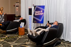 Person testing massage chair at conference vendor booth.
