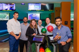 Group gathering at bowling alley with colorful bowling balls and scoring screens.