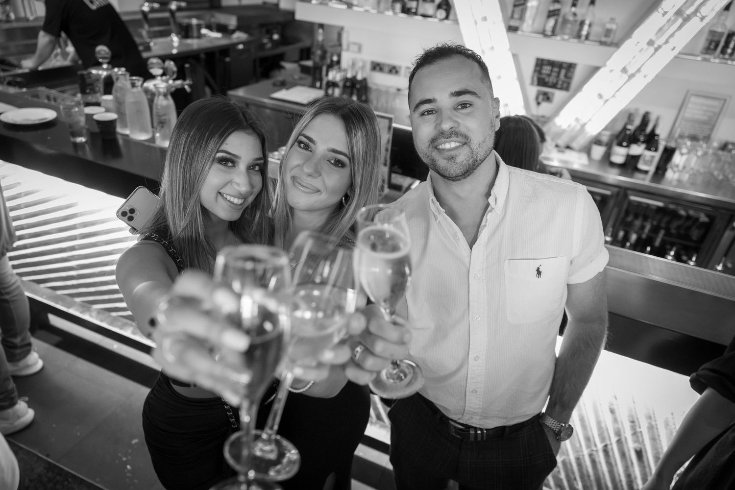 Sydney Event Photography - Friends celebrate with wine glasses at a modern bar counter in black and white photography.