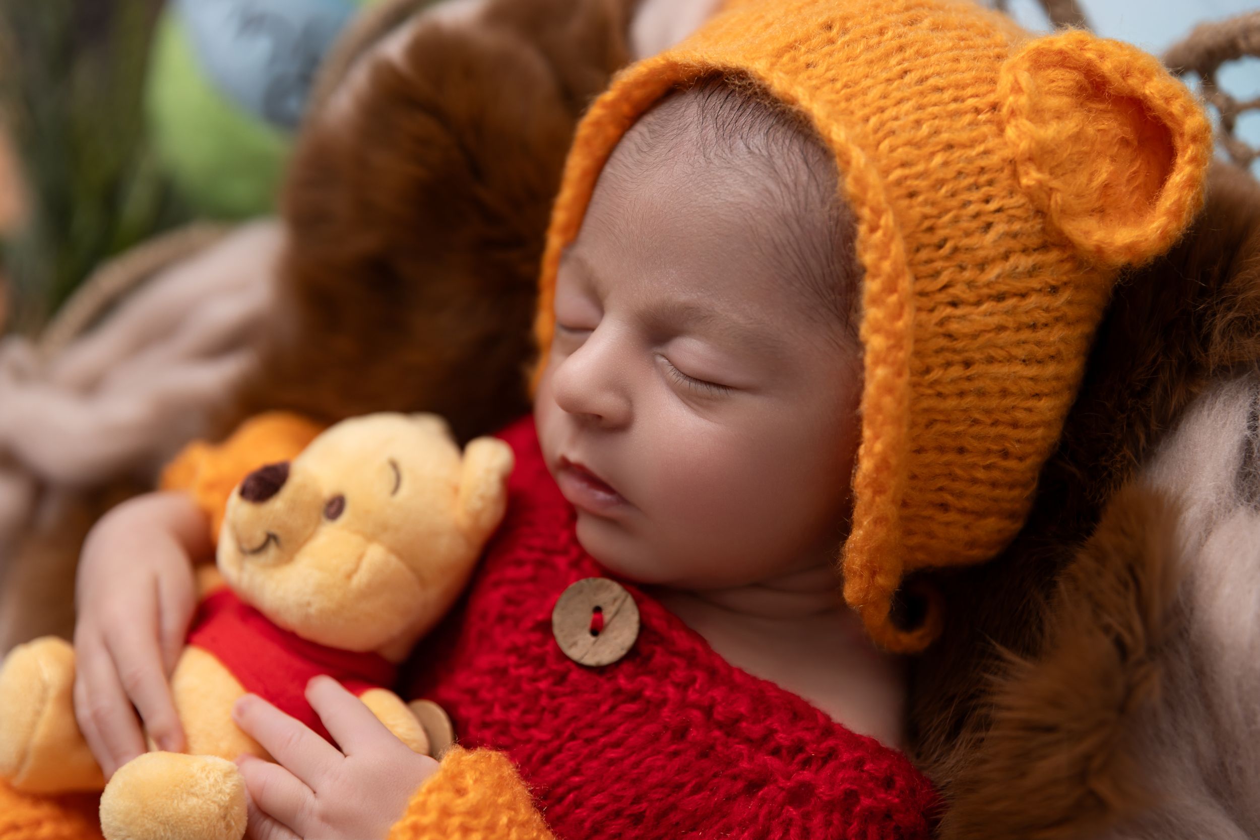 A sleeping baby wearing an orange knit hat cuddles with a soft Winnie the Pooh plush toy.