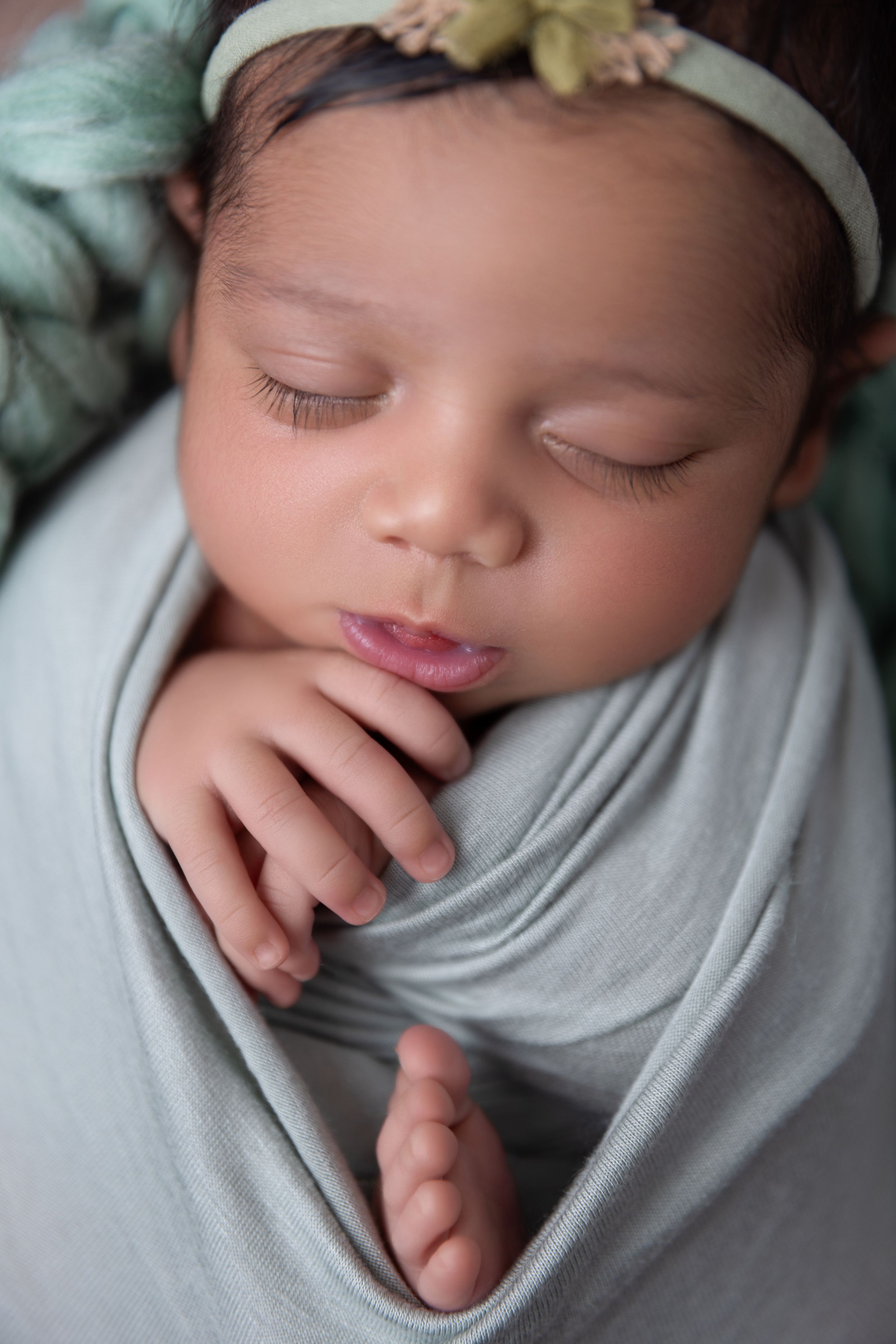 Sweet sleeping newborn baby wrapped in soft gray swaddle with tiny hands peeking out during professional photo session.