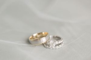 Two wedding rings photographed on white fabric, one gold band and one sparkly engagement ring.