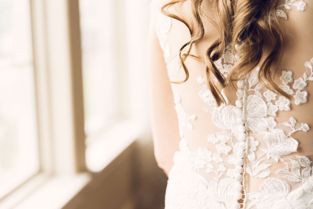 Close up detail of delicate lace and beadwork on a white wedding dress.
