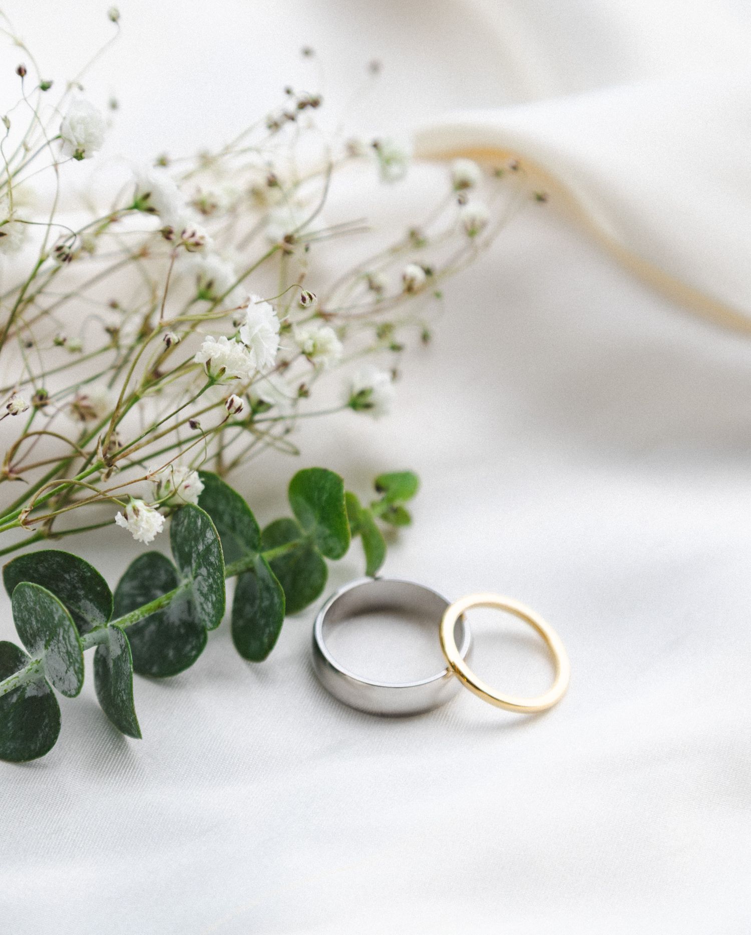 Wedding rings with eucalyptus leaves and baby's breath on white fabric.