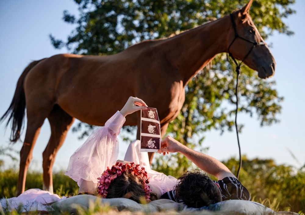 Expectant mother and father posing outdoors with a horse in the background, capturing a rustic maternity moment.