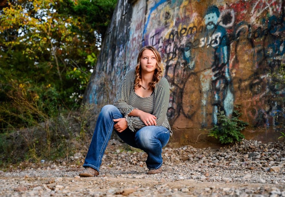 Senior looking off into the distance in front of a graffiti bridge.