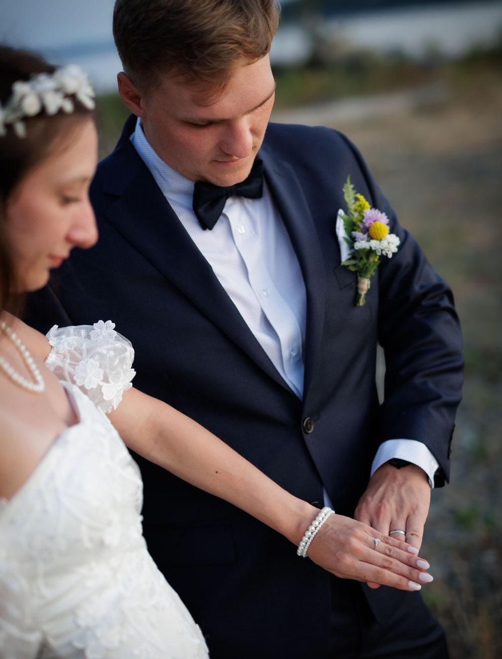 Bride and groom examining wedding rings outdoors at dusk in formal attire.