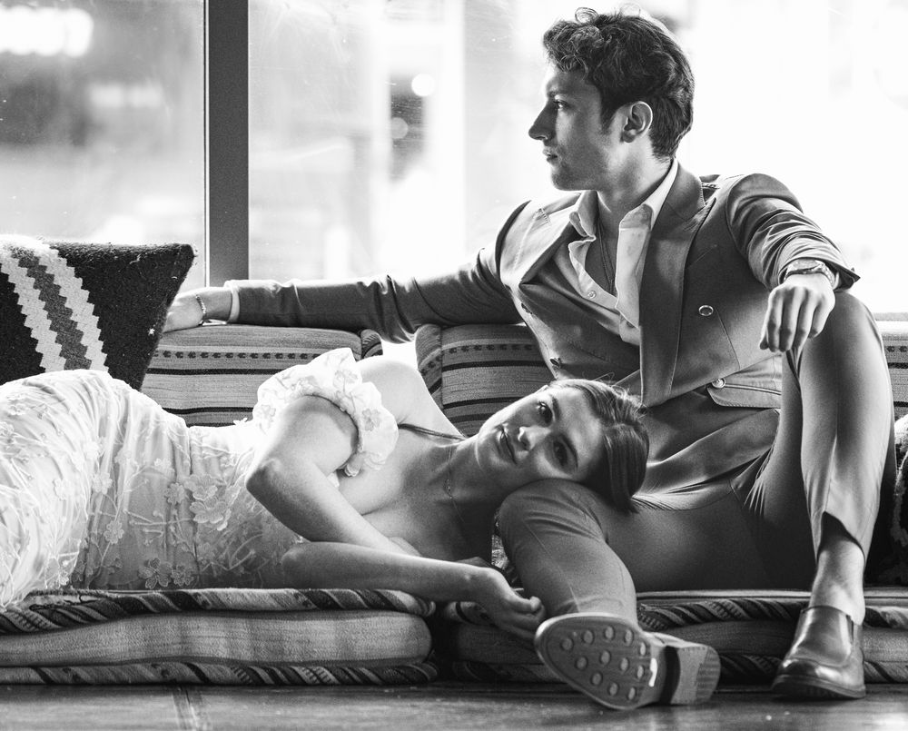 Black and white photo of couple posing on couch in elegant formal attire.