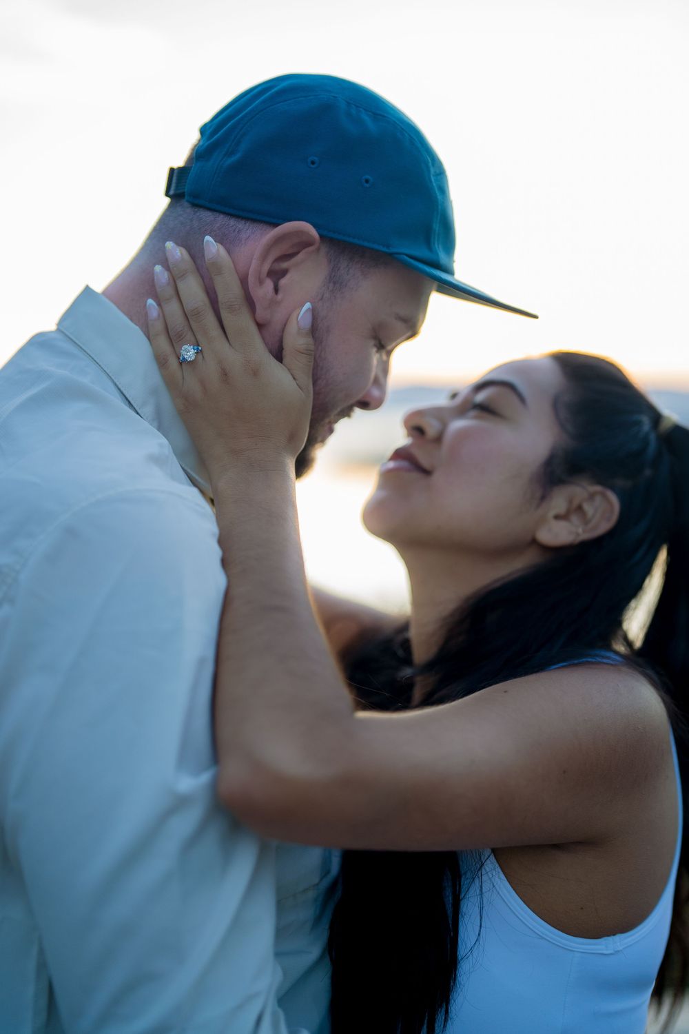 A couple shares an intimate moment together at sunset, with the person wearing a blue cap leaning in for a kiss.