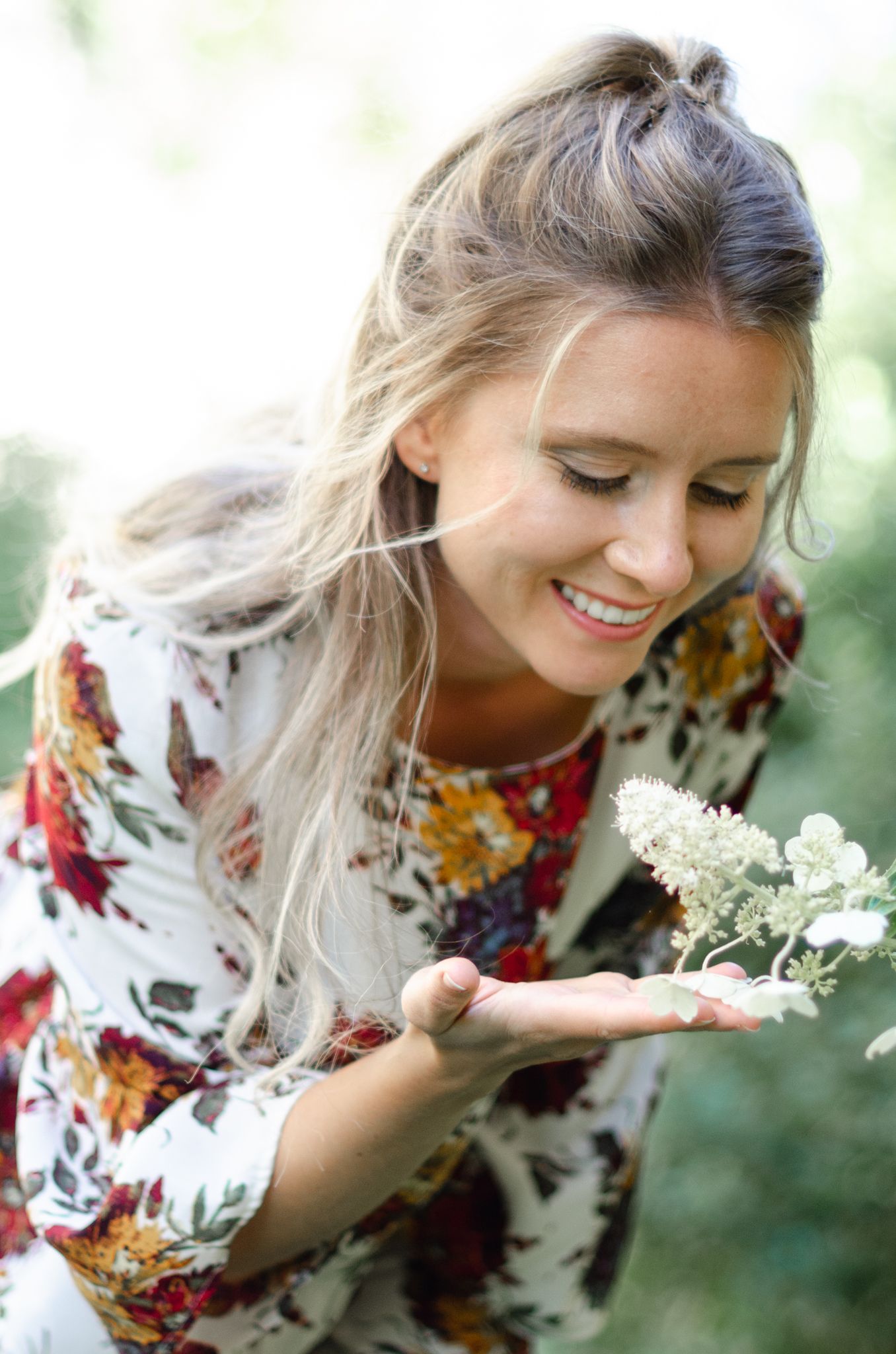 Someone in a floral dress admires white wildflowers in their hand on a sunny day.