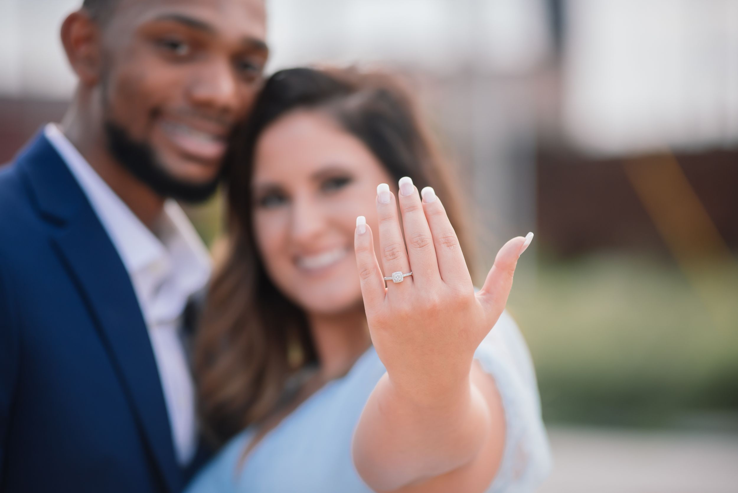 Smiling couple showing off an engagement ring up close after a proposal.
