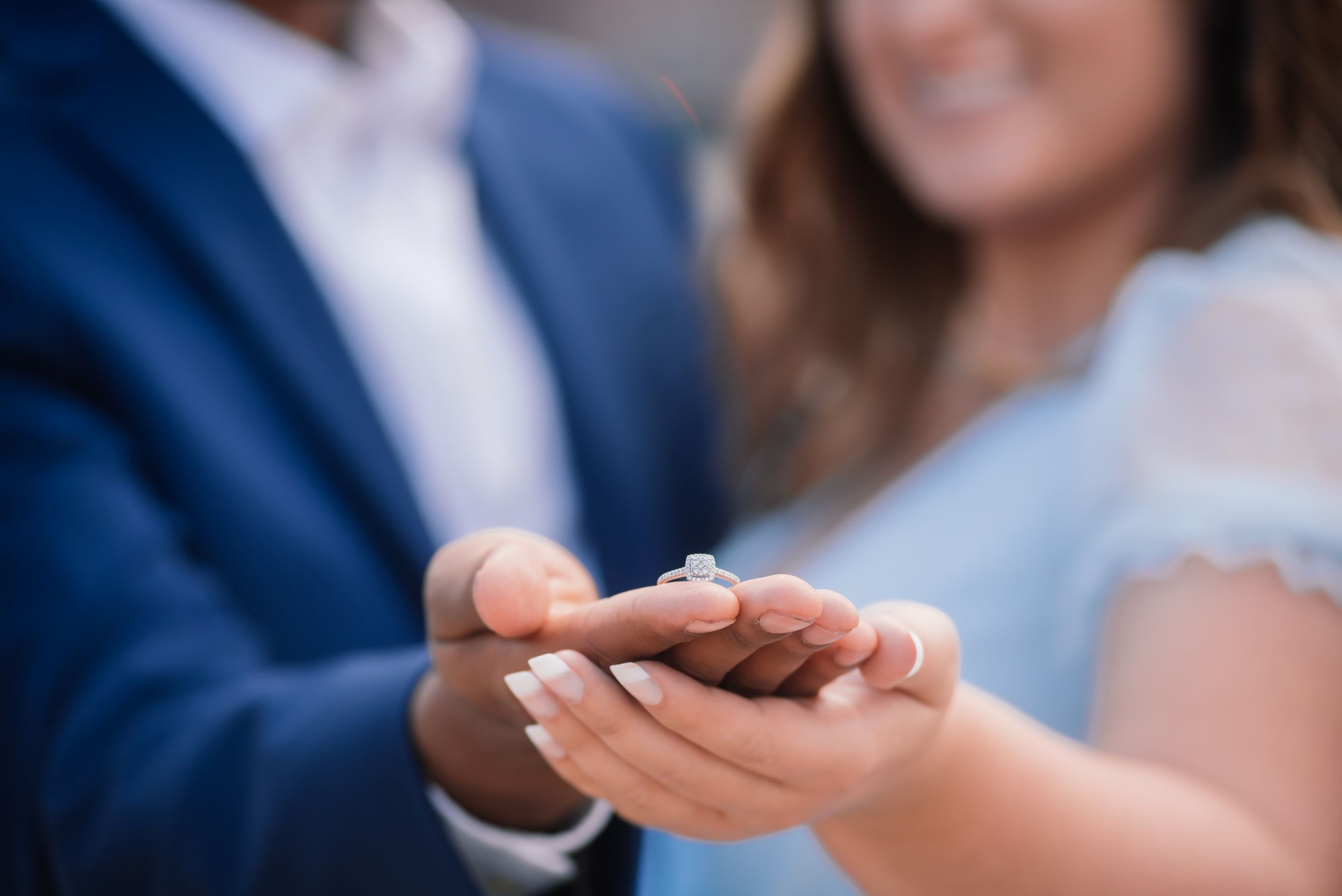 Close-up of an engaged couple holding a diamond engagement ring together in their hands.