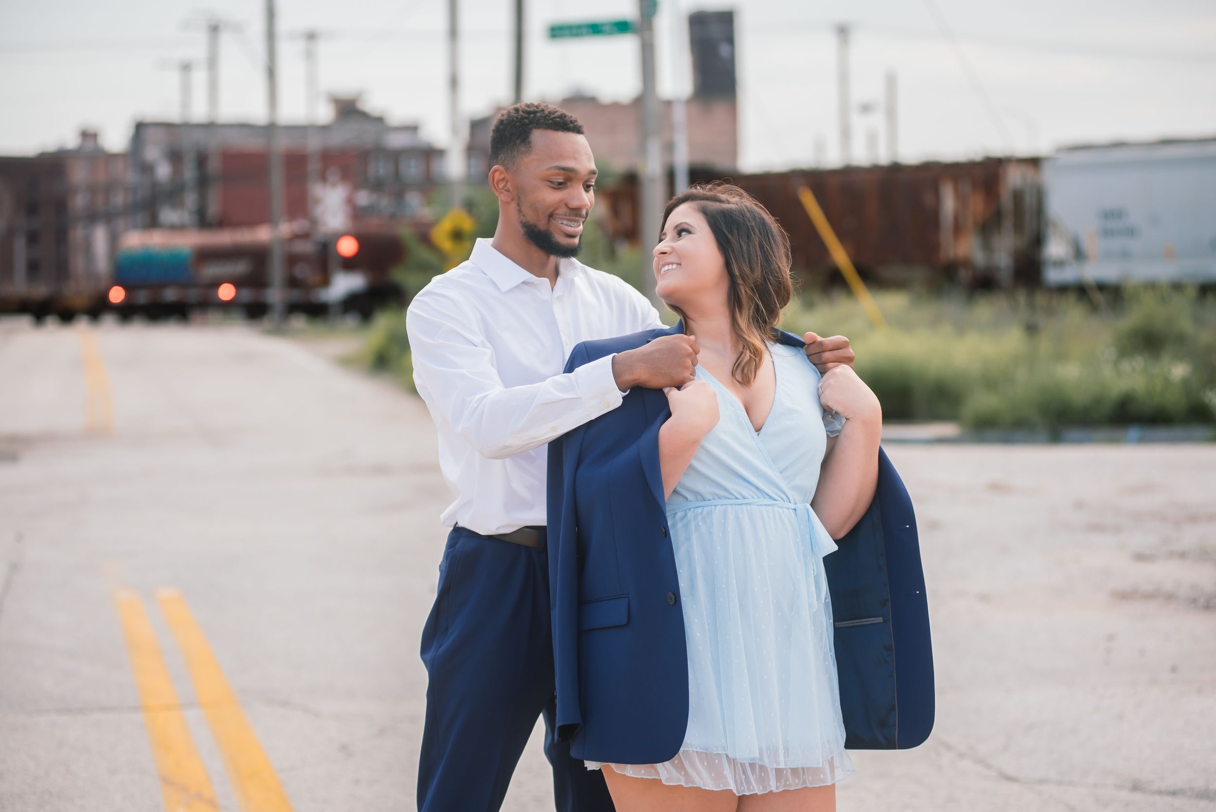 Couple sharing a sweet moment on a road, man draping his blue jacket over her shoulders.