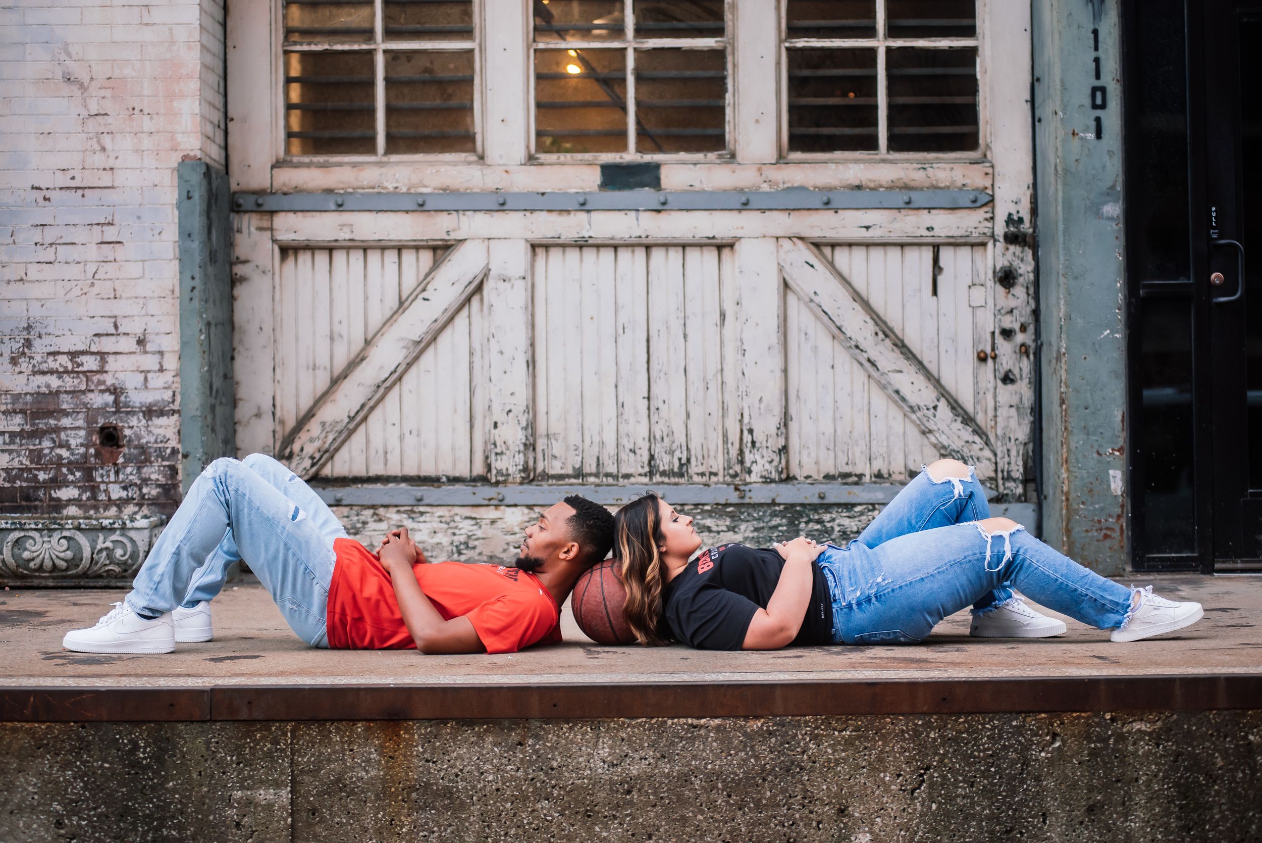 Casual couple lying head-to-head on an outdoor ledge in jeans, laughing together.