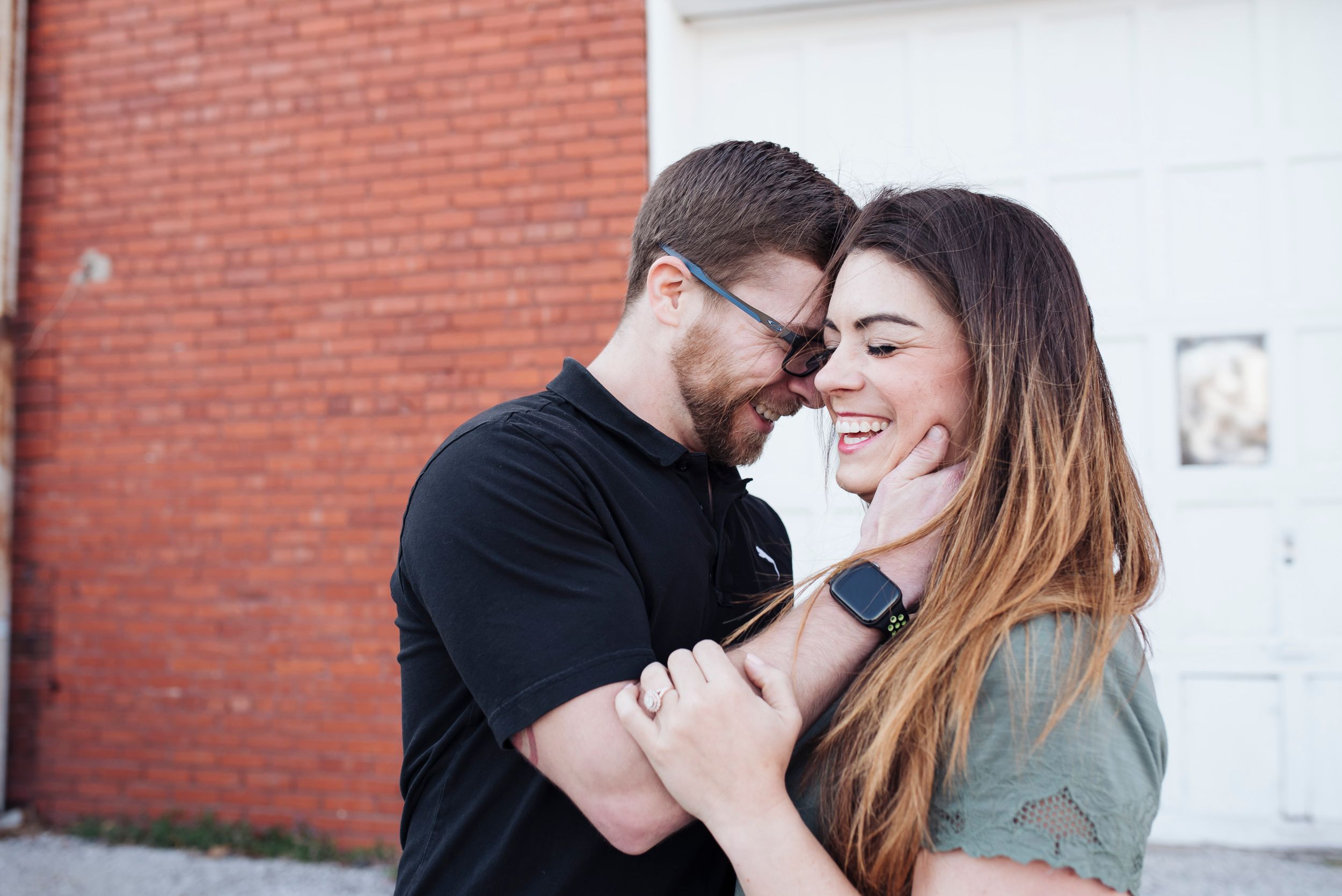 Happy couple laughing and embracing in front of a red brick wall.