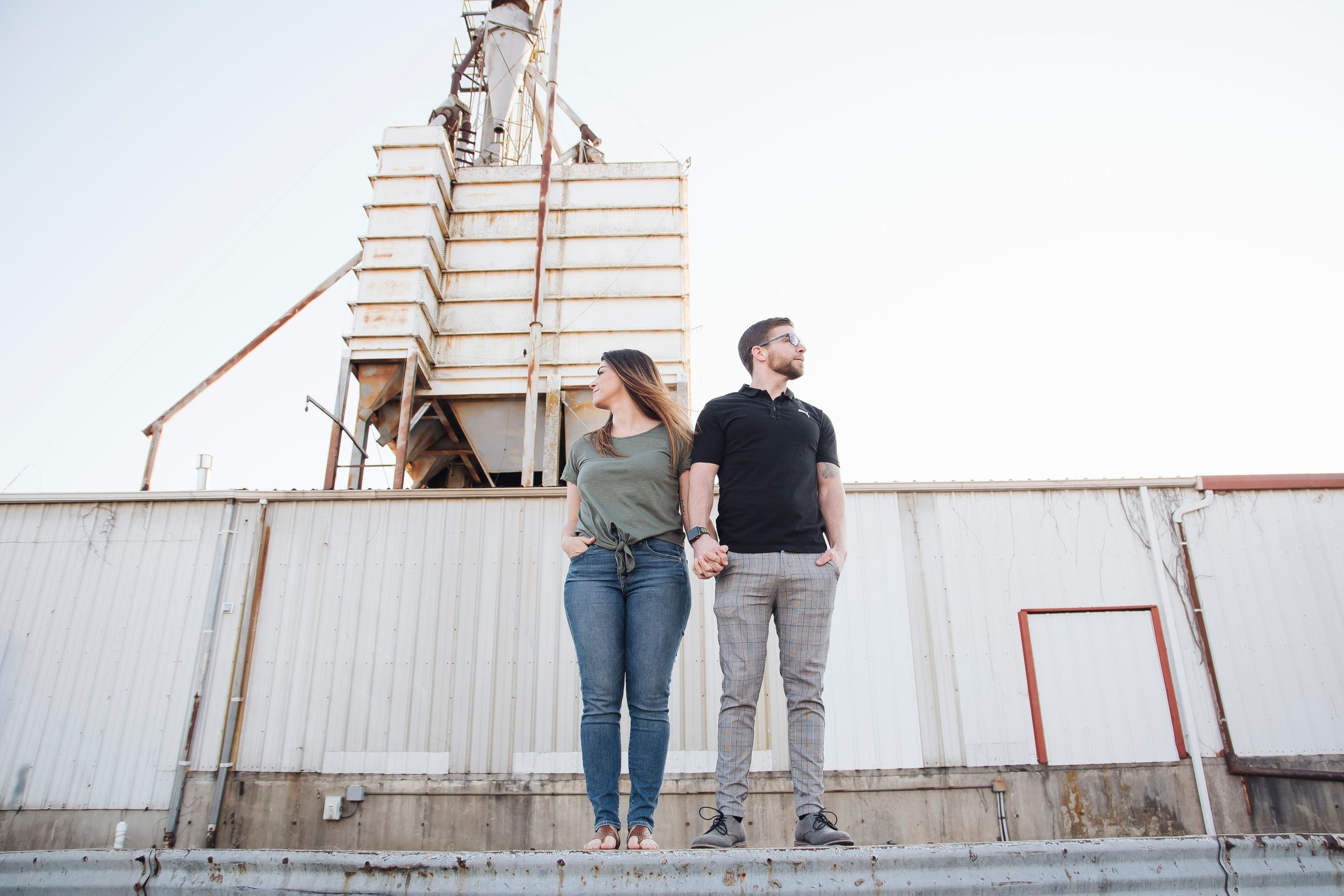 Couple holding hands standing near an industrial grain elevator outdoors.