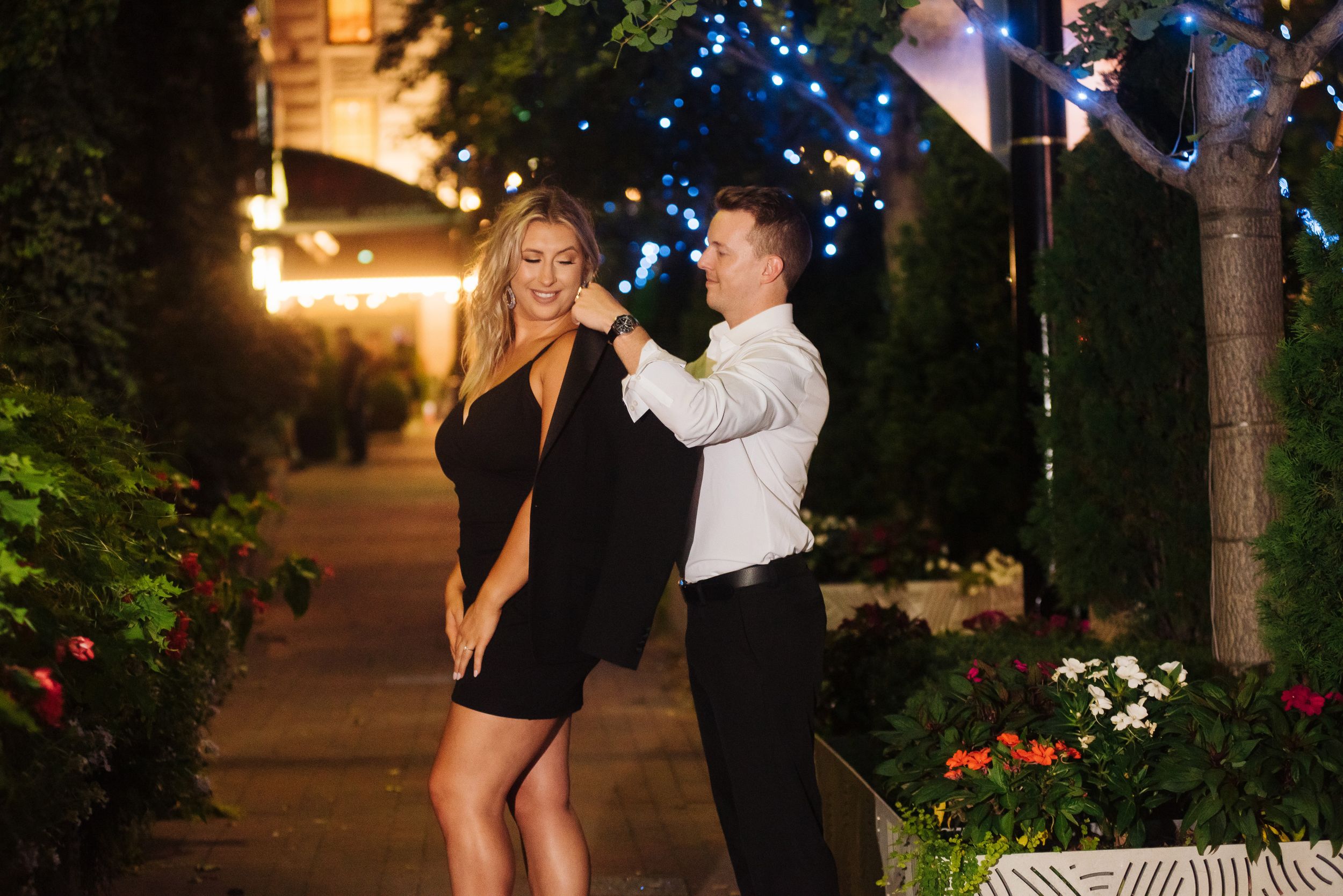 Couple dancing and laughing together on a garden pathway lit by string lights at night.