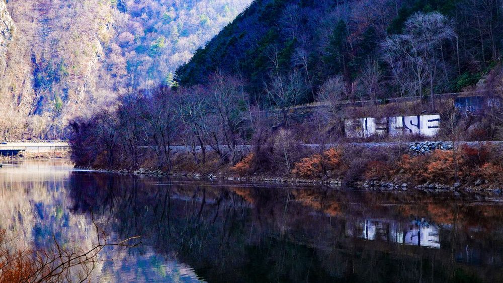 Winter landscape of a lake reflecting mountains and buildings in purple-tinted scenery.