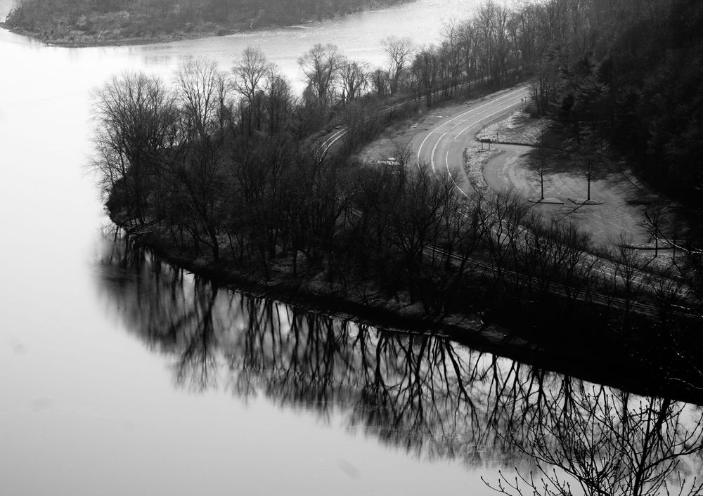 Aerial black and white view of a curving river with tree reflections on the water surface.