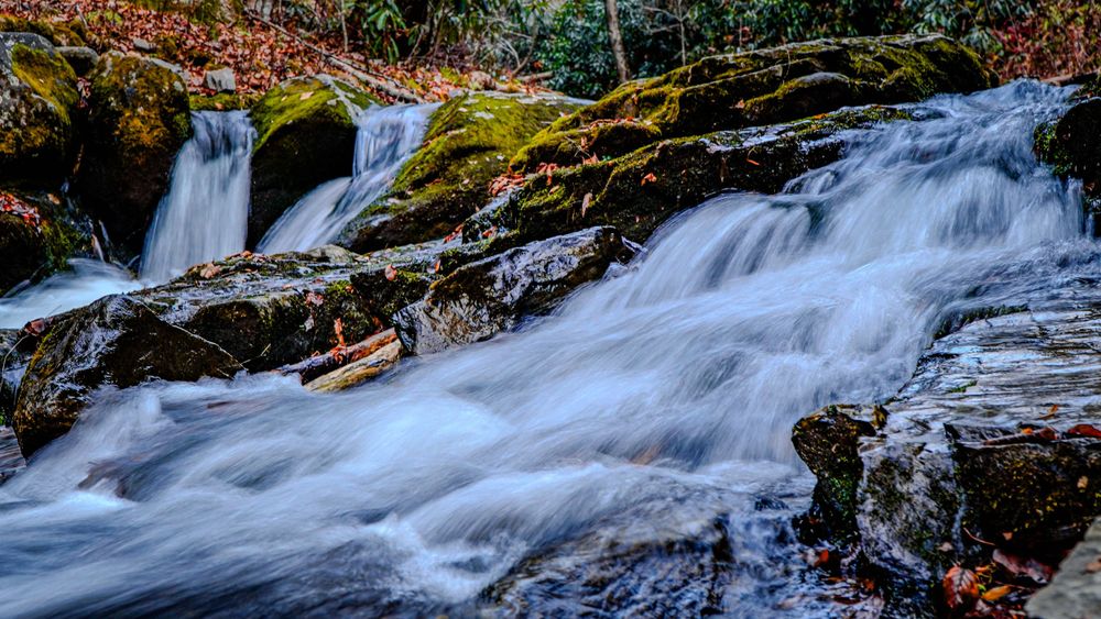 Cascading waterfall flowing over moss-covered rocks in a forest setting.