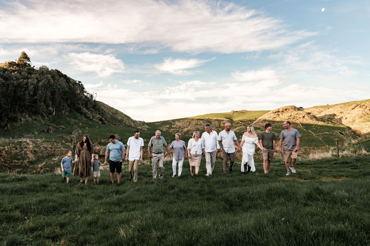 Group walking together across grassy hillside under blue sky.