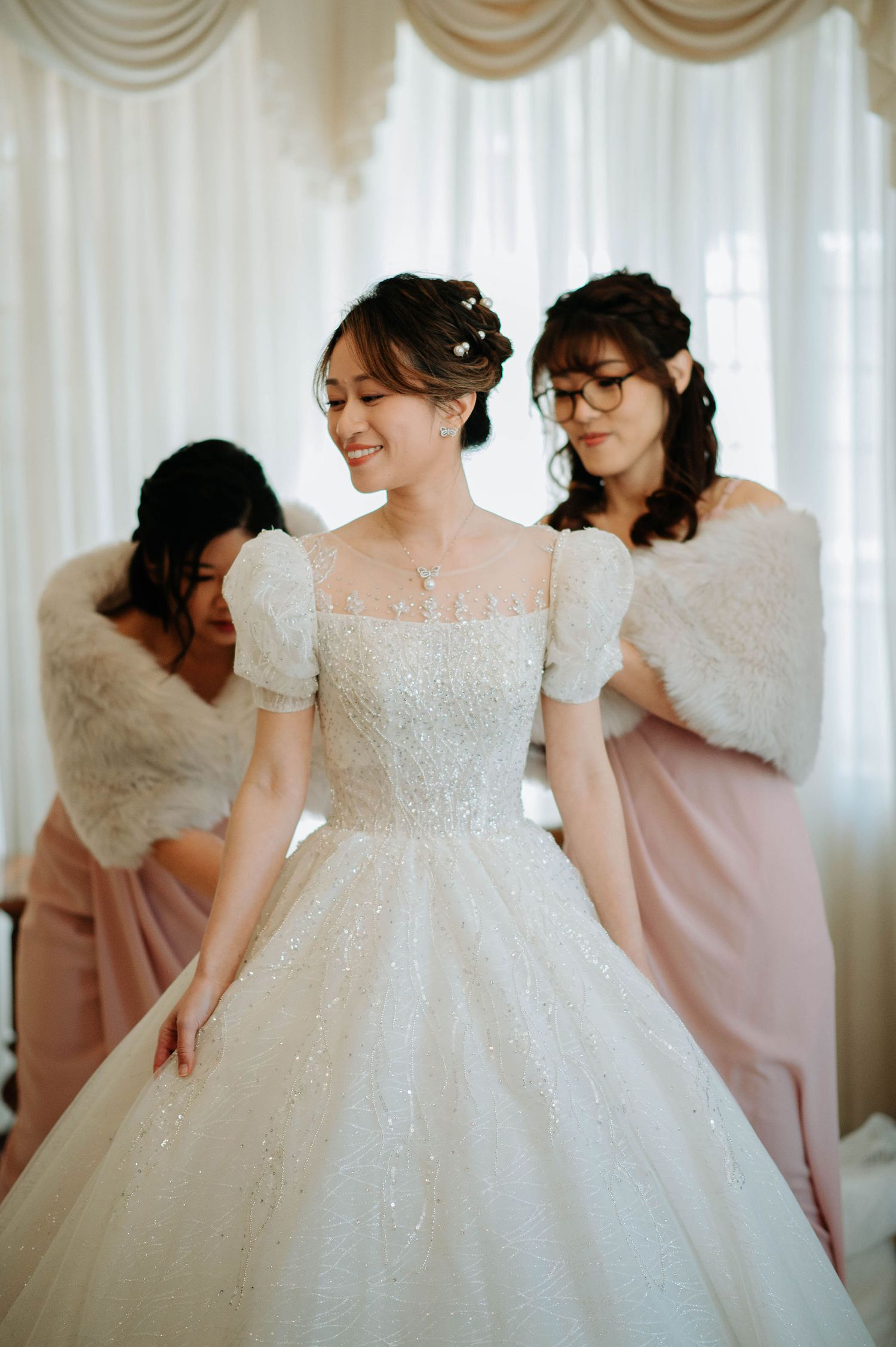 Bride in sparkly ballgown with bridesmaids in pink and white fur wraps.
