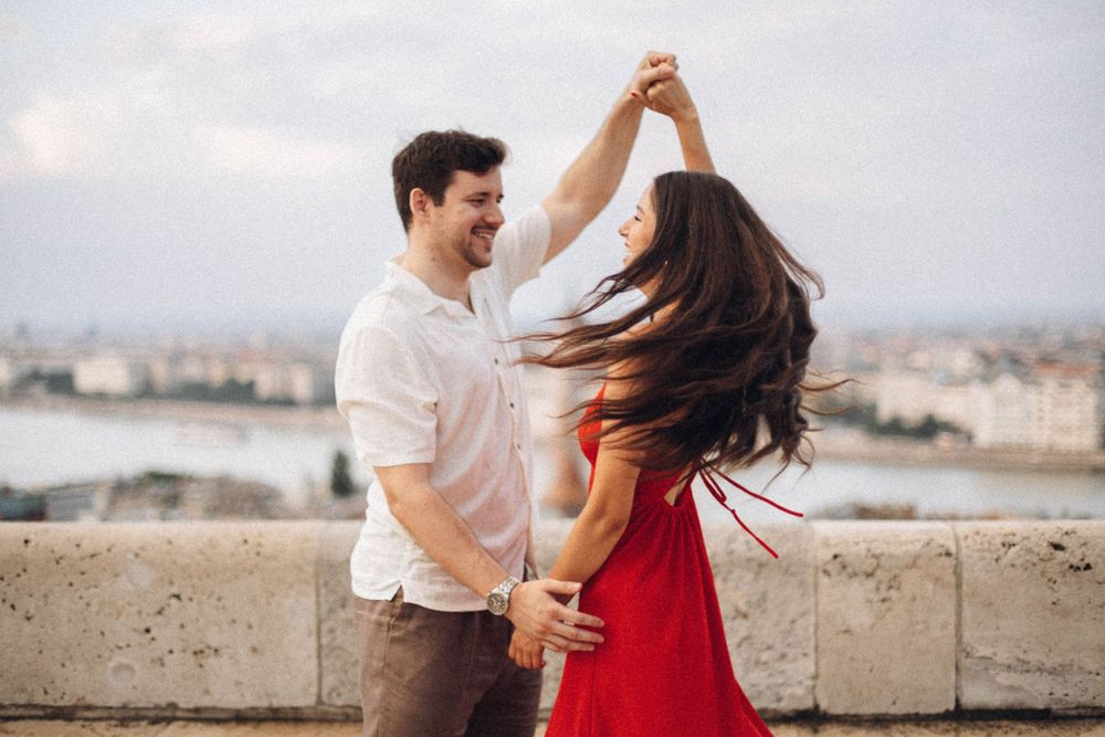 A happy couple twirls together on a Budapest terrace with the city skyline and Parliament in the background.