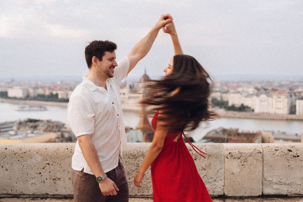 A joyful couple dances and twirls on a scenic Budapest overlook with the Parliament visible behind them.