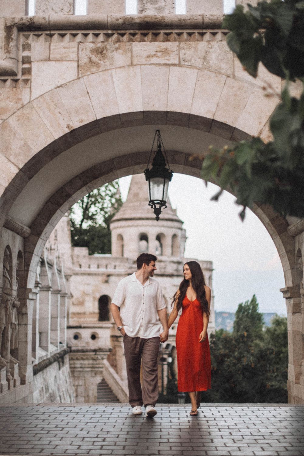 Couple holding hands walking under a stone arch at Fisherman's Bastion in Budapest.