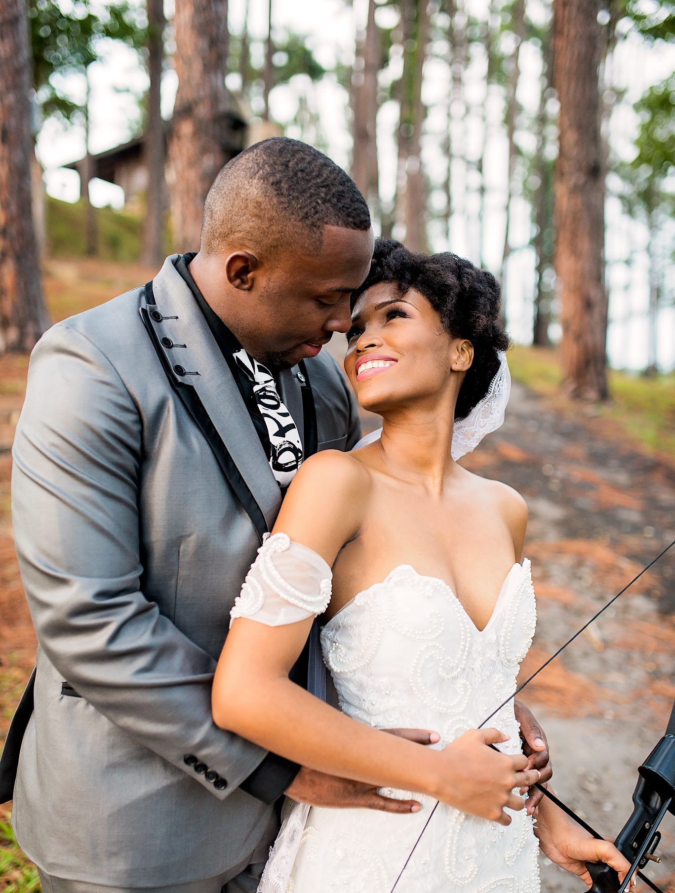 Romantic forest wedding portrait with couple embracing among tall pine trees.