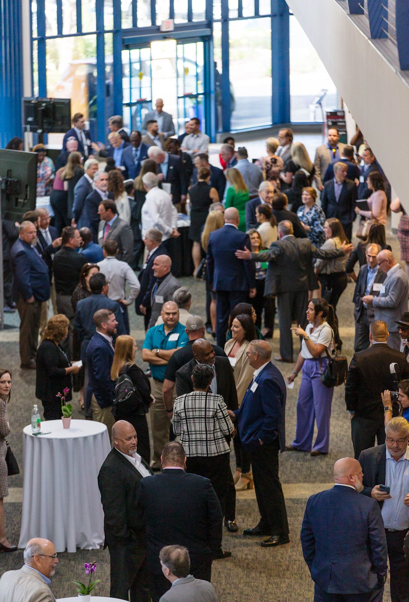 Large crowd of business professionals networking at corporate event with cocktail tables.