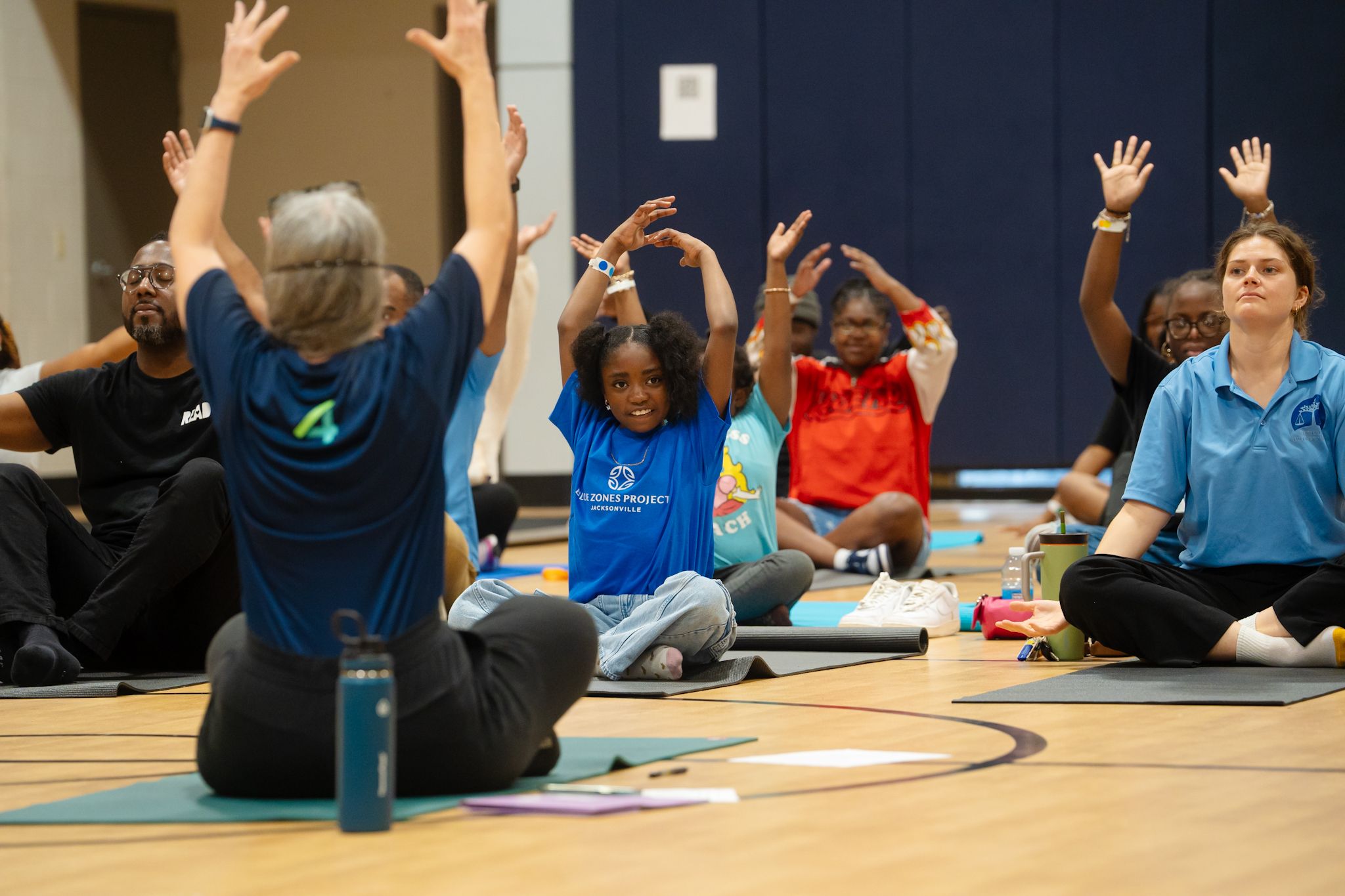 People participating in a group exercise class with raised arms in a gymnasium.