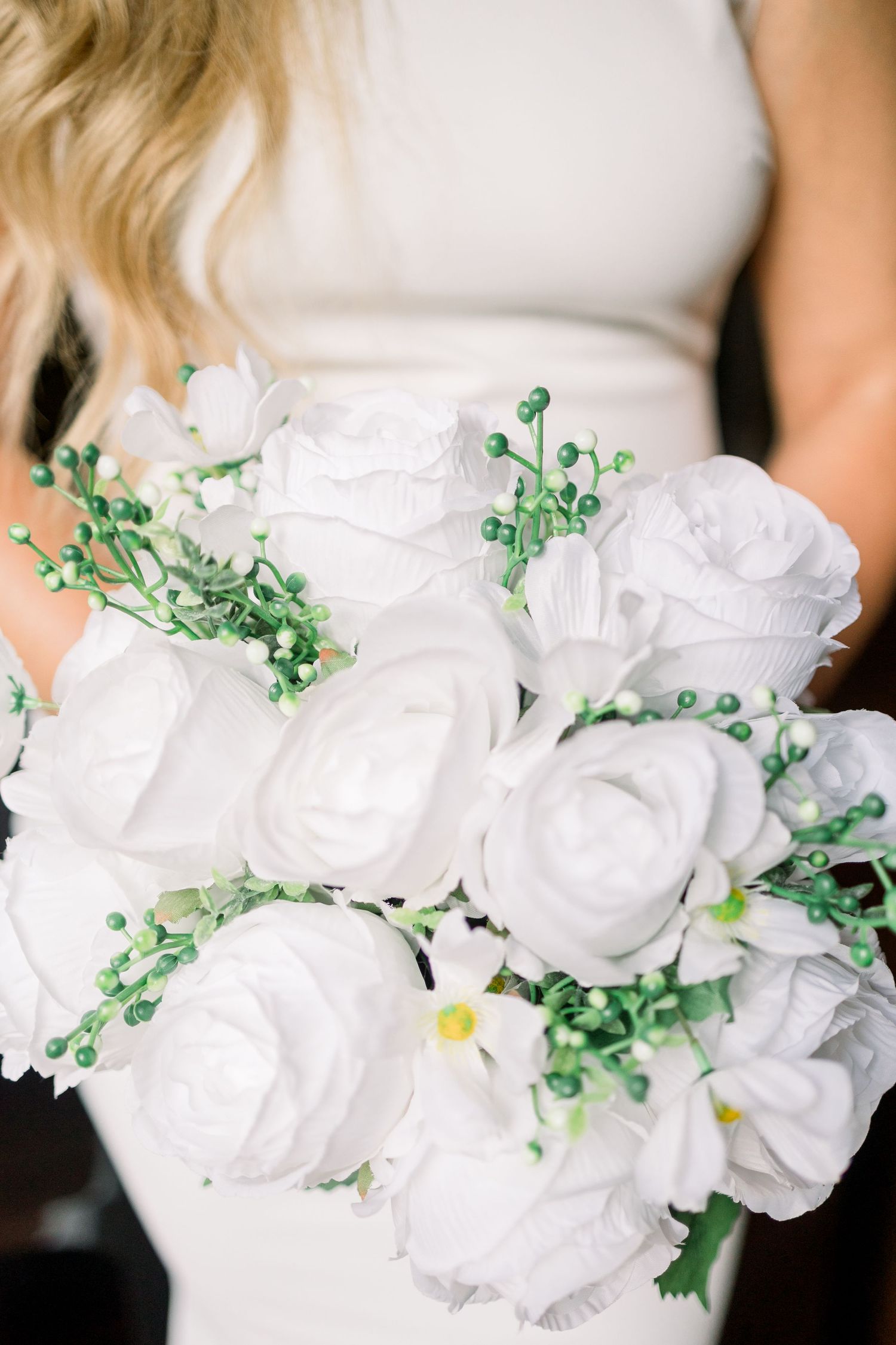 Beautiful white rose bouquet with delicate green accents against white dress.