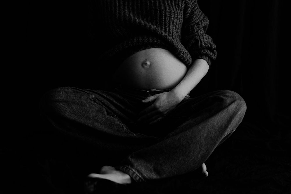 Black and White pregnant lady sitting with legs crossed showing baby bump, in studio in Greymouth