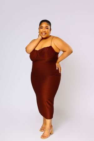 Fashion model in a brown bodycon dress striking a confident pose against a studio background.