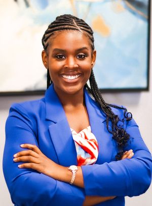 Professional portrait of a person in a royal blue blazer with arms crossed, smiling confidently.