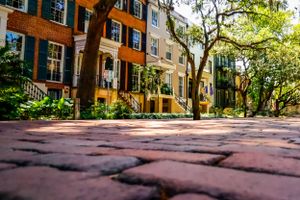 Low angle view of brick walkway leading to historic townhouses with black shutters and stoops.