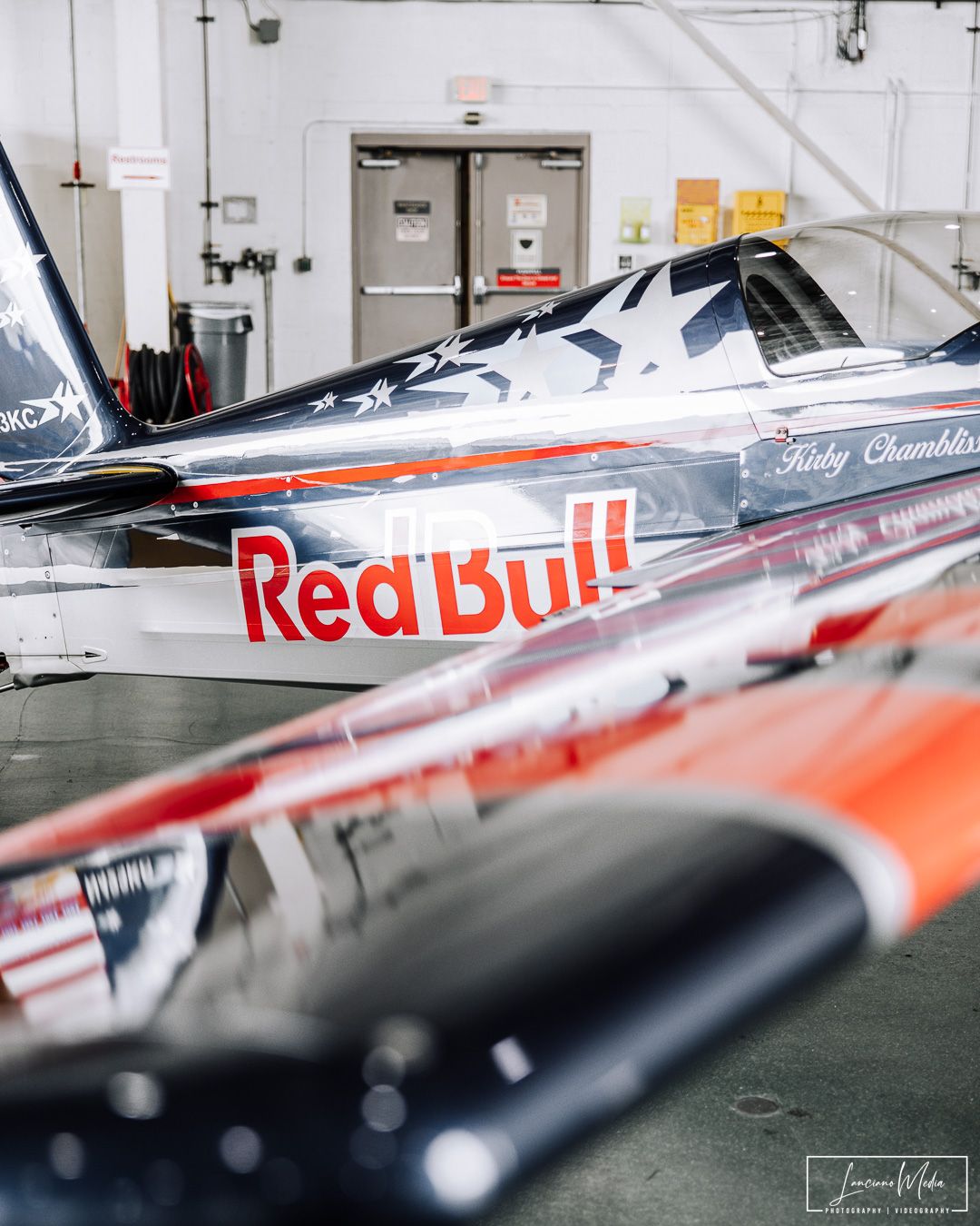 A Red Bull racing aircraft parked inside an aircraft hangar with its distinctive livery visible.