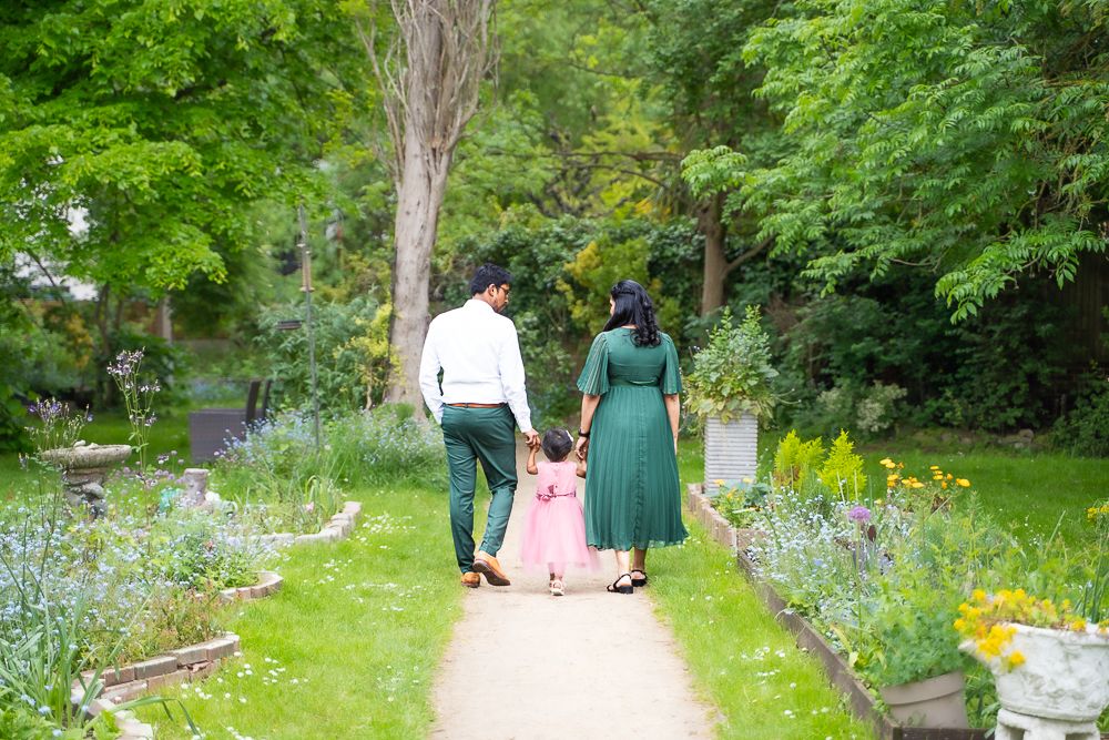 Family walking together on a garden path surrounded by lush greenery and flowering plants.