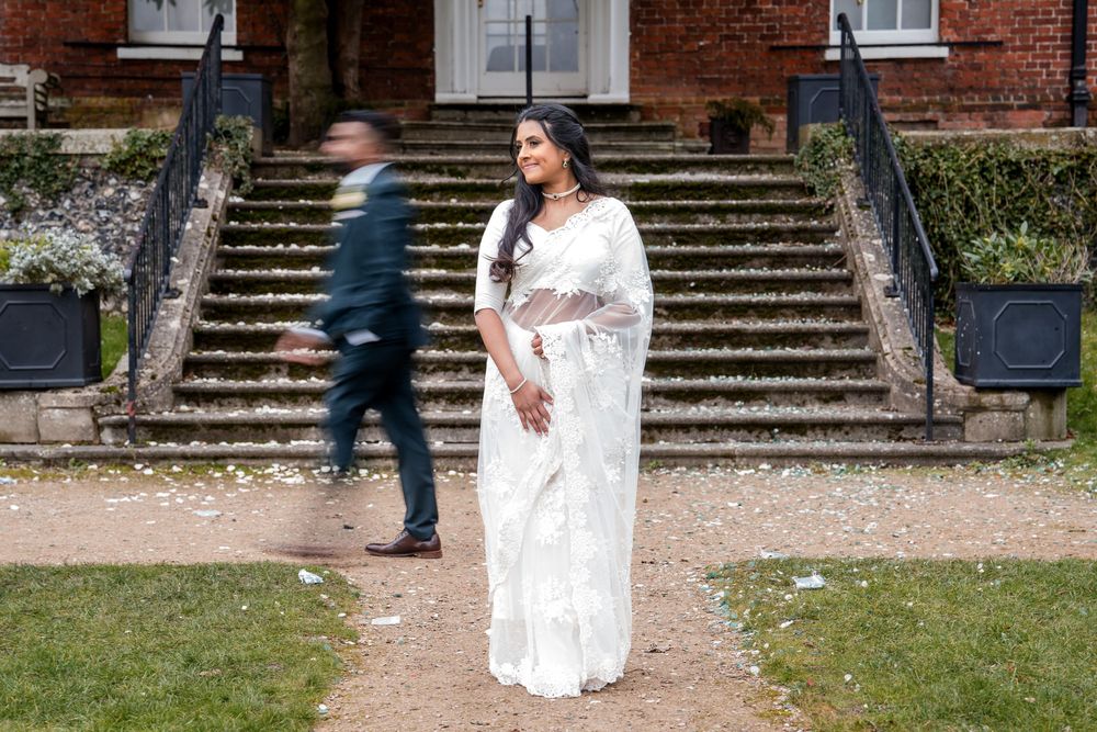 A person in a white lace sari stands in front of stone steps at a historic building while another figure walks past.