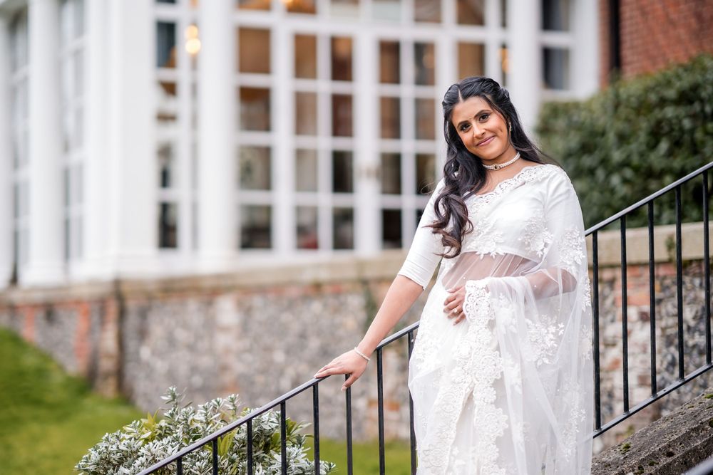 Elegant white lace saree worn on outdoor stone steps with brick and window architecture in background.