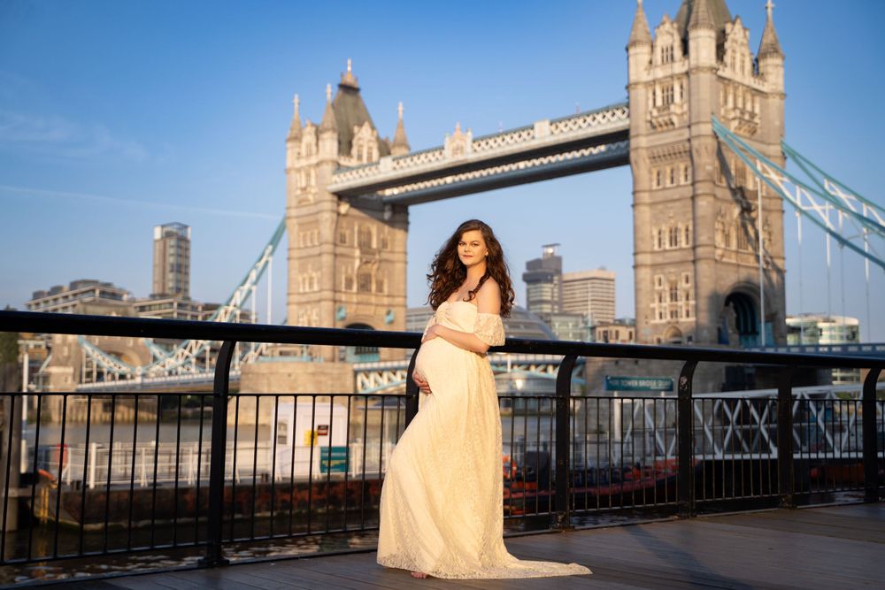 A yellow dress-clad figure poses against the iconic Tower Bridge in London during golden hour for her maternity photoshoot.