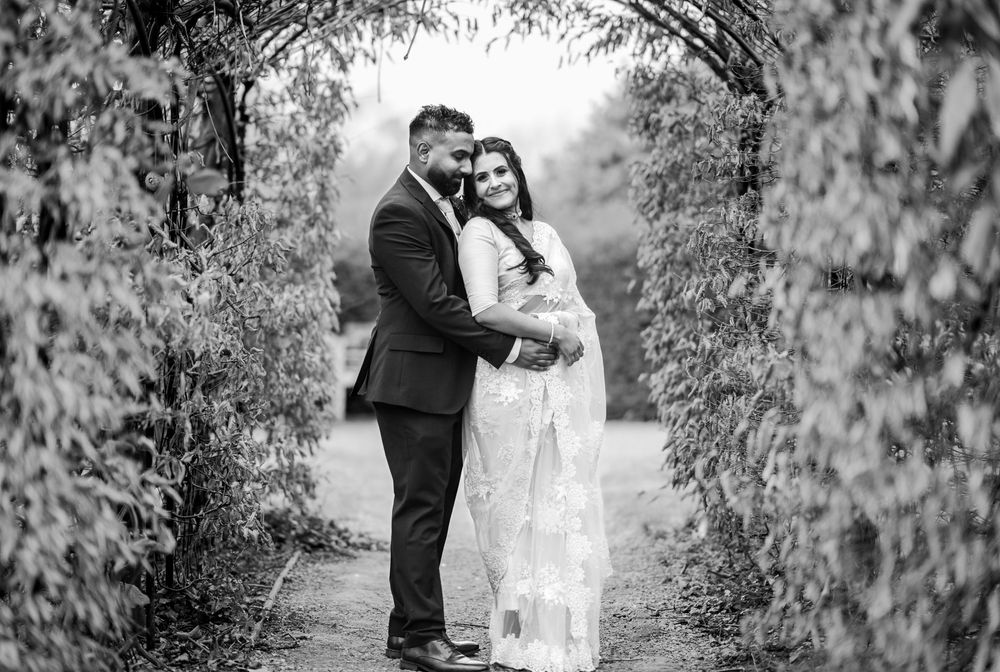 A romantic couple embraces under a garden archway surrounded by lush foliage in black and white photography.