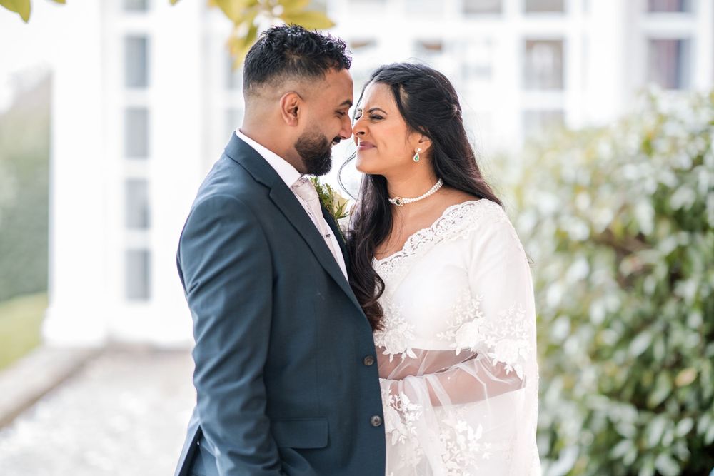 A couple shares a romantic moment together outdoors in formal wedding attire with sunlit buildings in the background.
