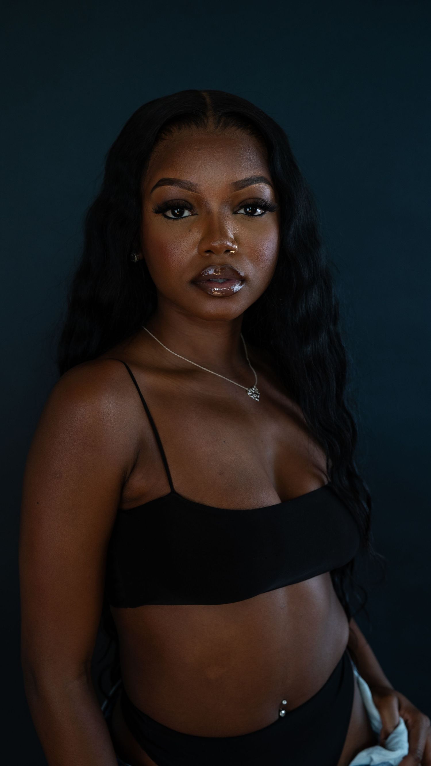 Studio fashion portrait with black crop top and flowing dark hair against deep blue background.