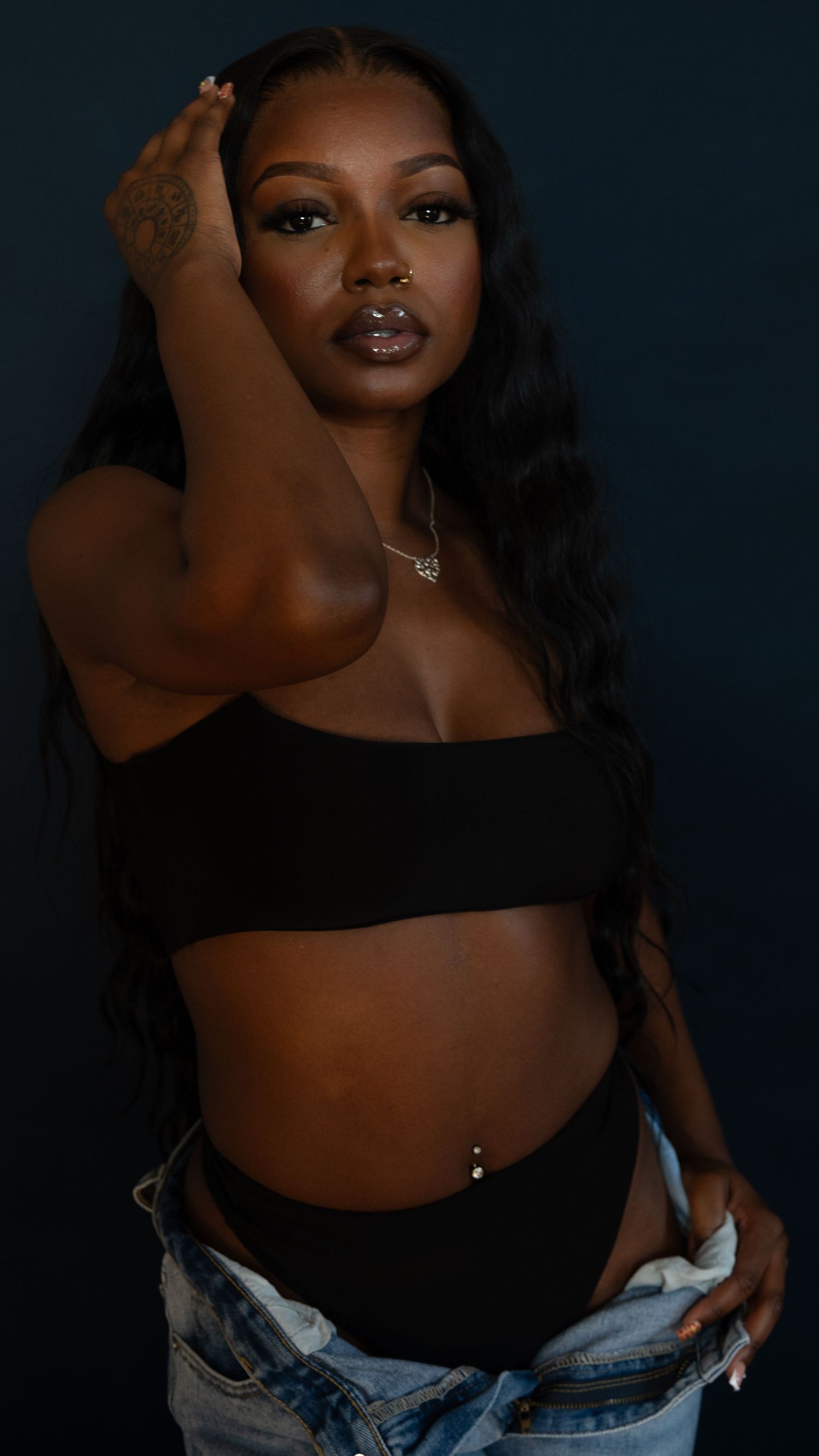 Glamour portrait in black crop top and denim with moody lighting and artistic makeup.