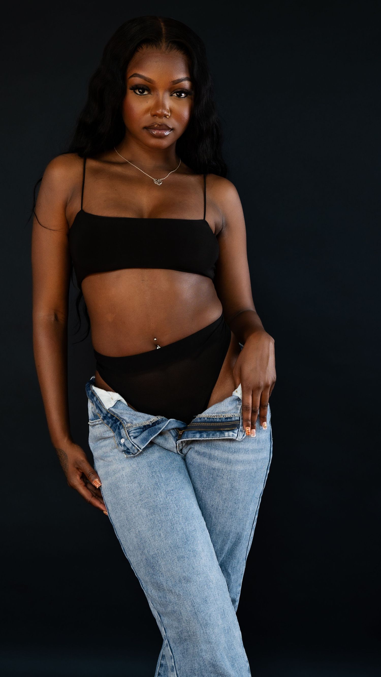 Modern fashion portrait in black crop top and light wash denim with minimalist silver jewelry.