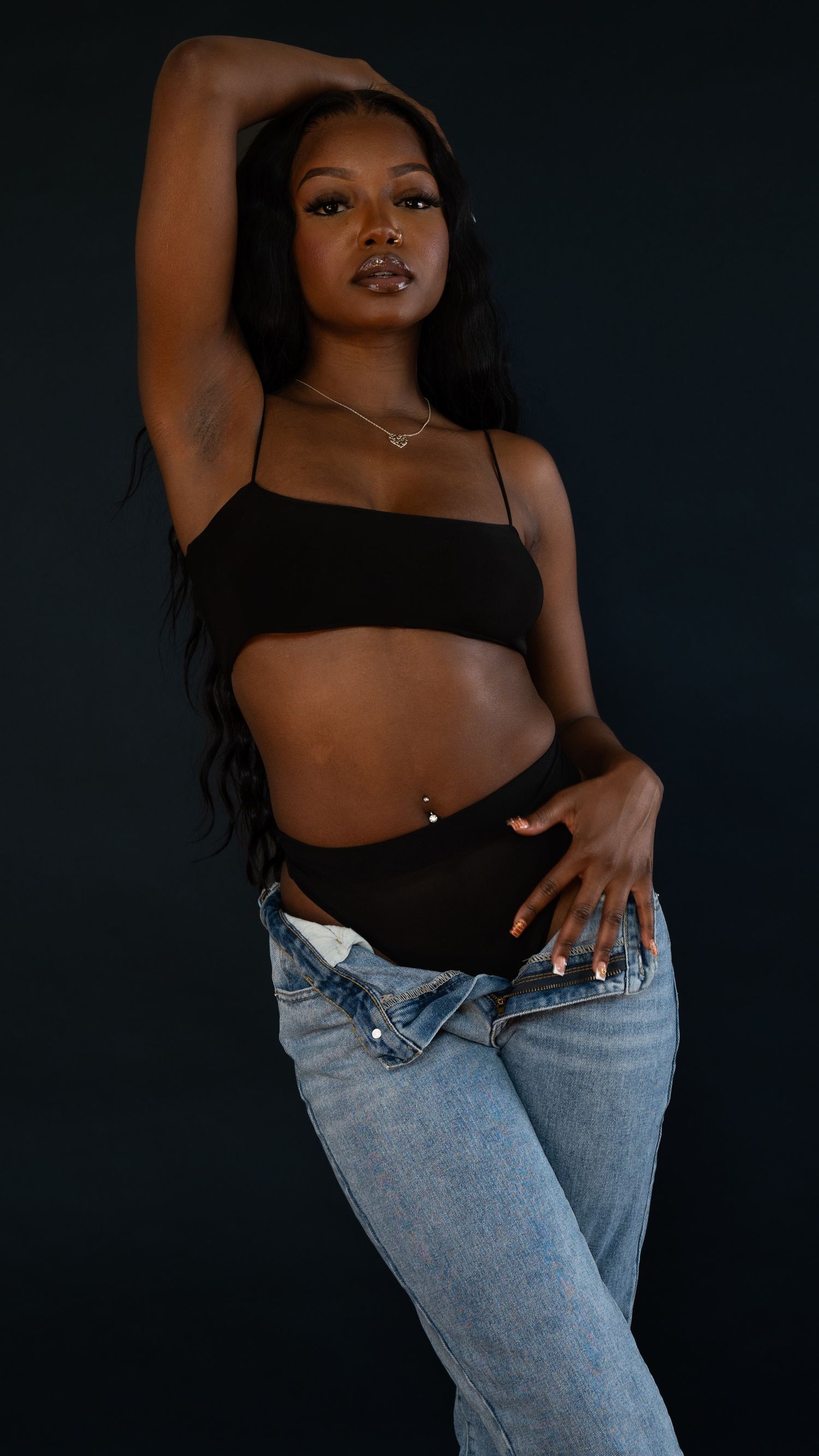 Fashion model poses confidently in casual black and denim outfit against dark studio backdrop.