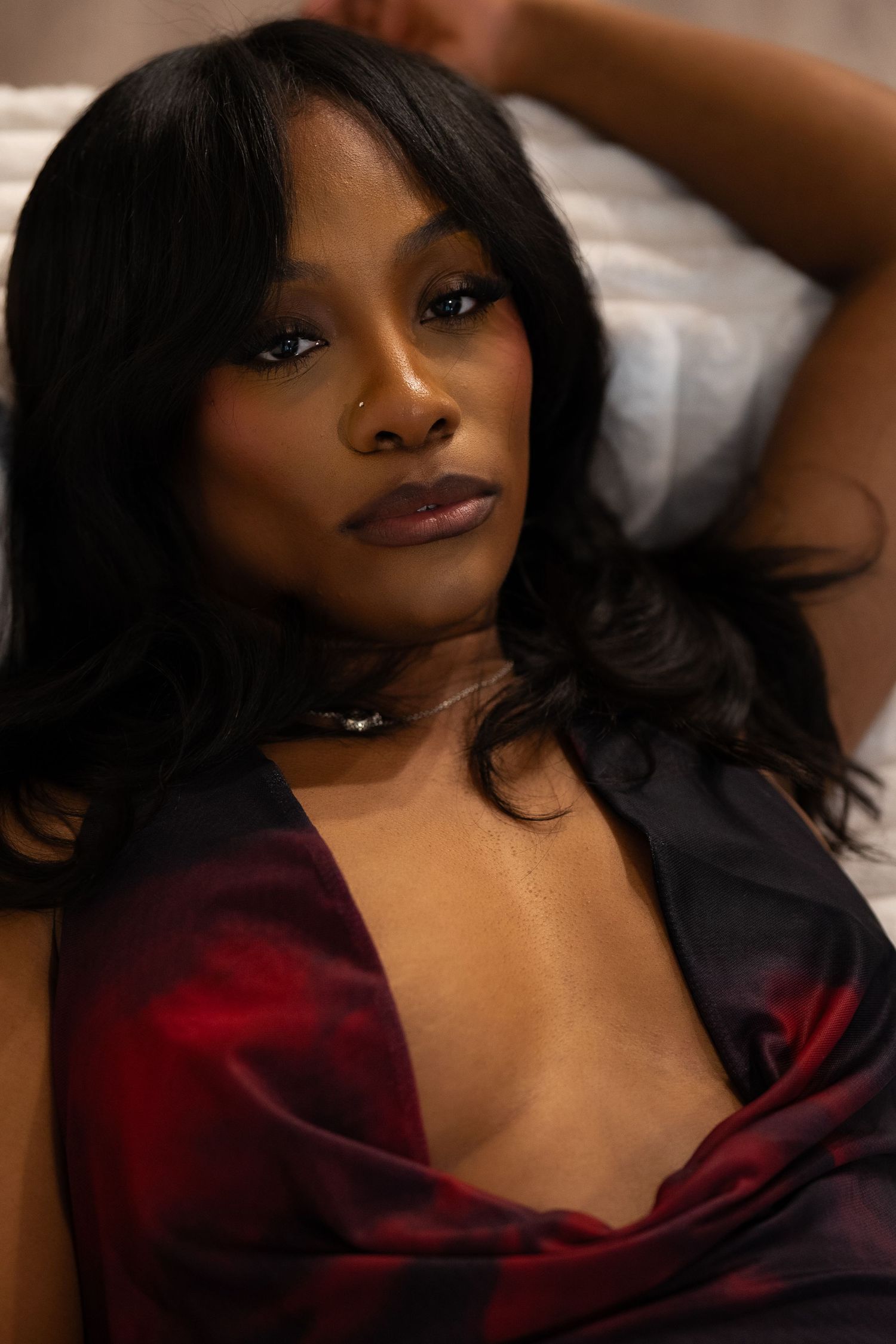 A woman in a burgundy satin robe poses seductively in a boudoir photoshoot.