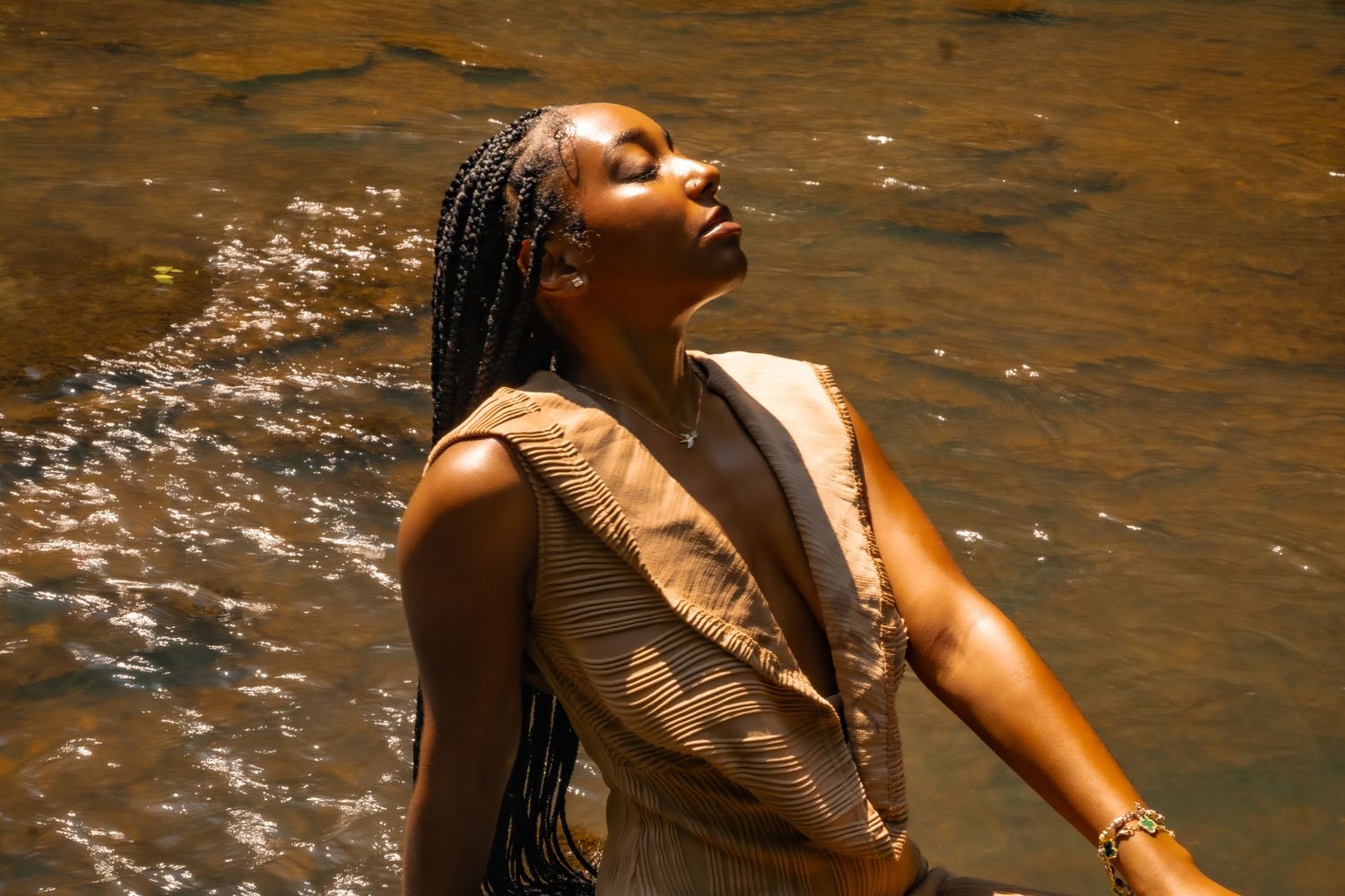 Artistic portrait in golden dress with water droplets creating ethereal effect in natural sunlight.